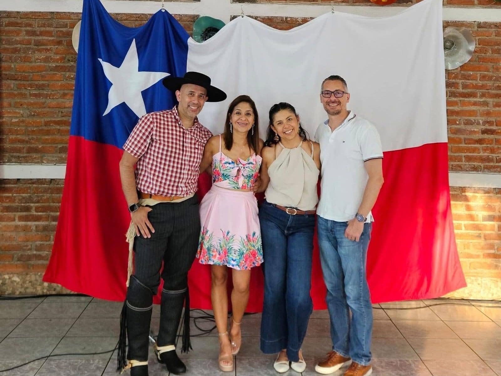 Cuatro asistentes posan frente a la bandera chilena; uno lleva el traje completo de huaso.